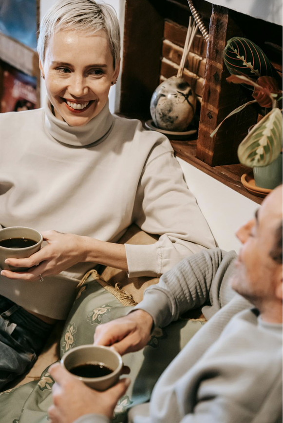 Couple with coffee cups on sofa looking at each other while conversing.