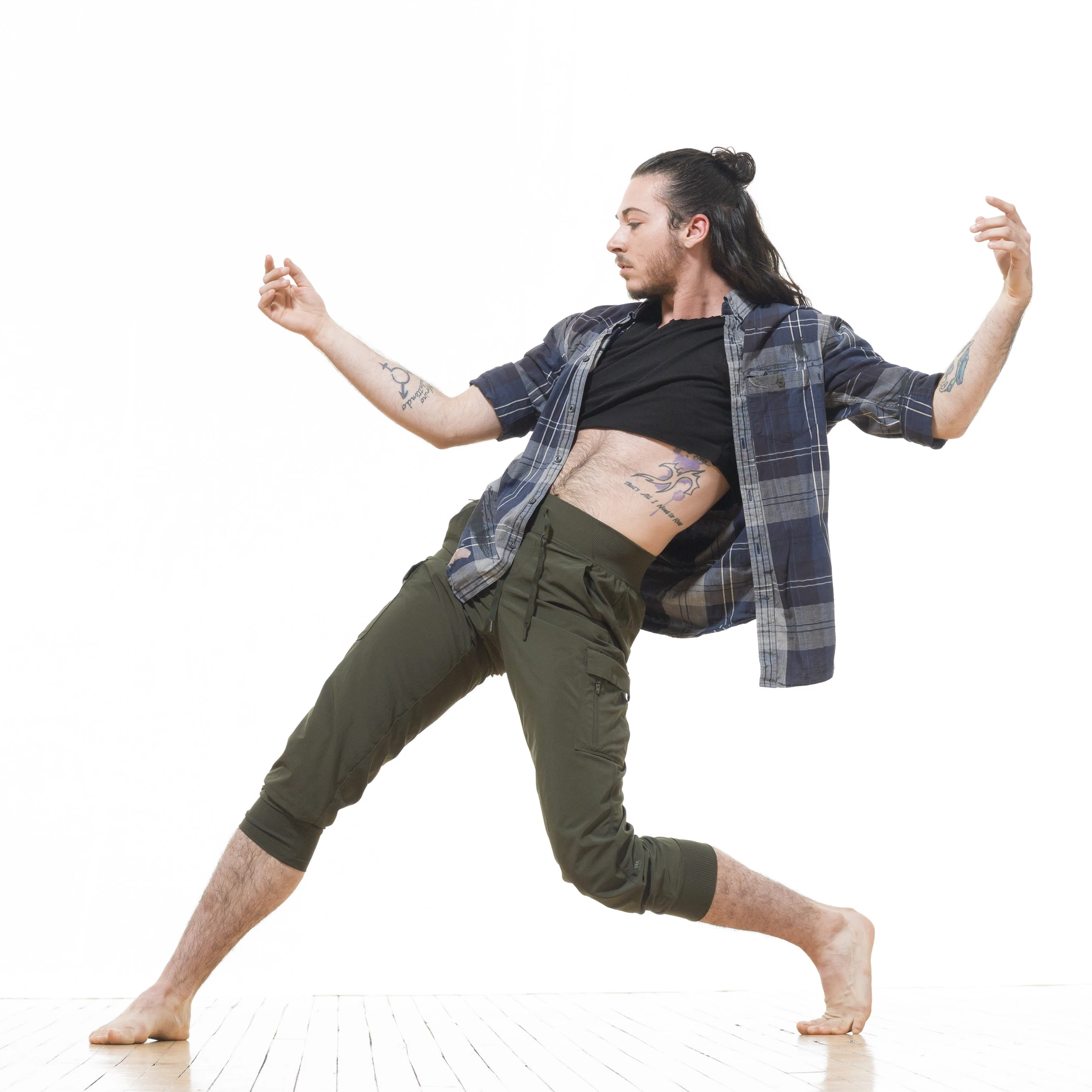 Luke poses against a white backdrop in green pants and an opened plaid shirt.