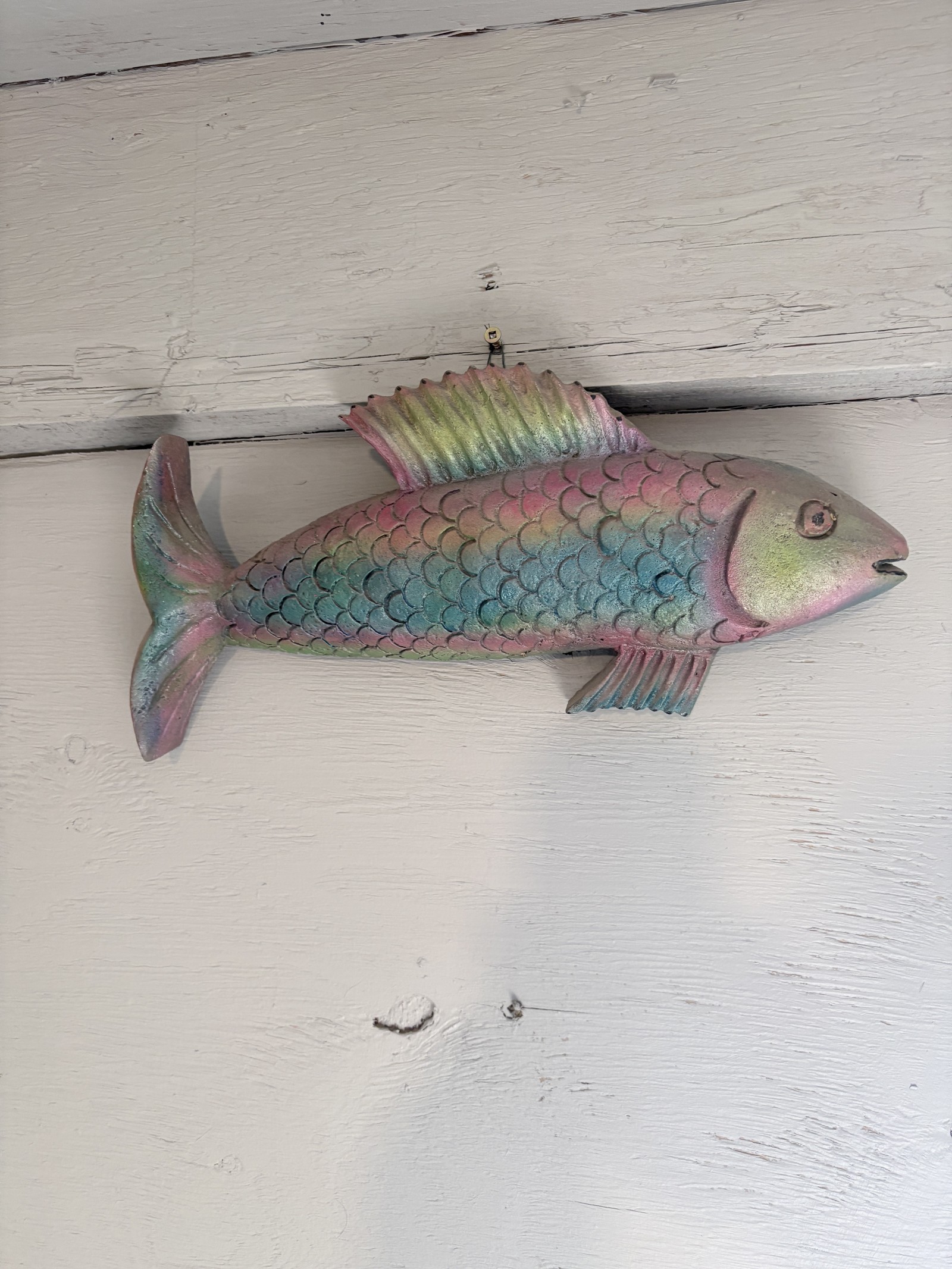 Handcrafted metal fish sculpture titled 'Fish' by Saskatoon artist Rik (Rick Luczka). This vibrant, recycled steel art piece features textured scales in shades of pink, green, and blue with a slightly open mouth. Created using an experimental sand-cast aluminum lost foam method, this unique Saskatchewan-made wall hanging is perfect for colorful home or office decor.