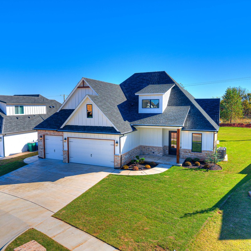 Aerial view of the completed custom home at 10408 SW 51st Street in Mustang Oklahoma showcasing the three-car garage, landscaped yard, and modern farmhouse design.