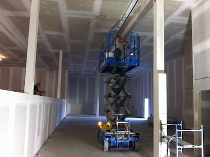 2 drywall technicians installing drywall in a toronto commercial space. One is on a lift and the other is working from the ground.
