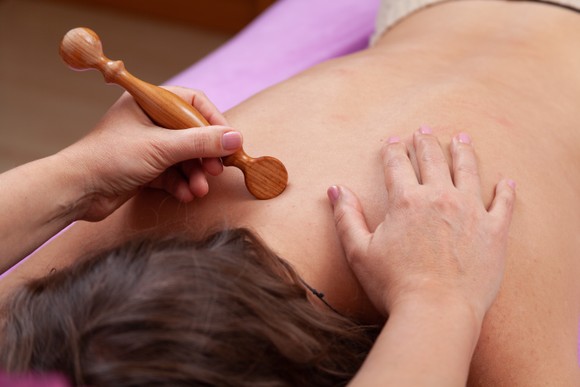 Therapeutin behandelt den Rücken einer Frau mit einem Holzlöffel bei der Bindegewebsmassage»