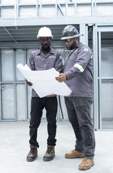 Two construction project managers standing in a steel-frame structure in development reading site drawing.