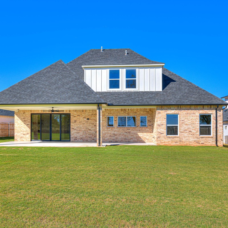 Full back view of the completed Mustang Oklahoma custom home with spacious lawn and brick exterior under a clear blue sky.