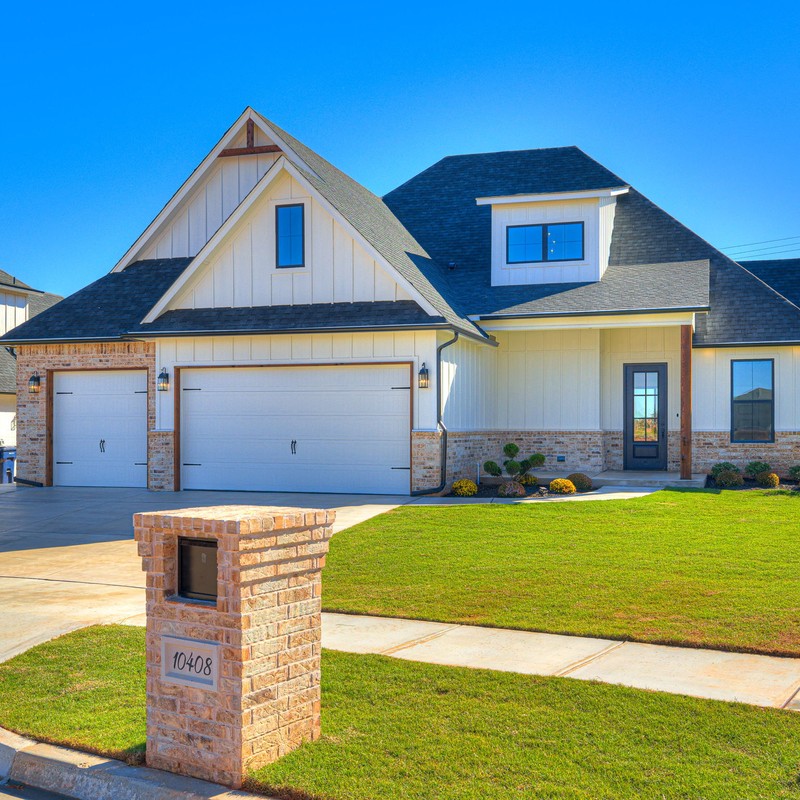 Front view of the custom home at 10408 SW 51st Street in Mustang Oklahoma showing the three-car garage, landscaped yard, and modern farmhouse design.