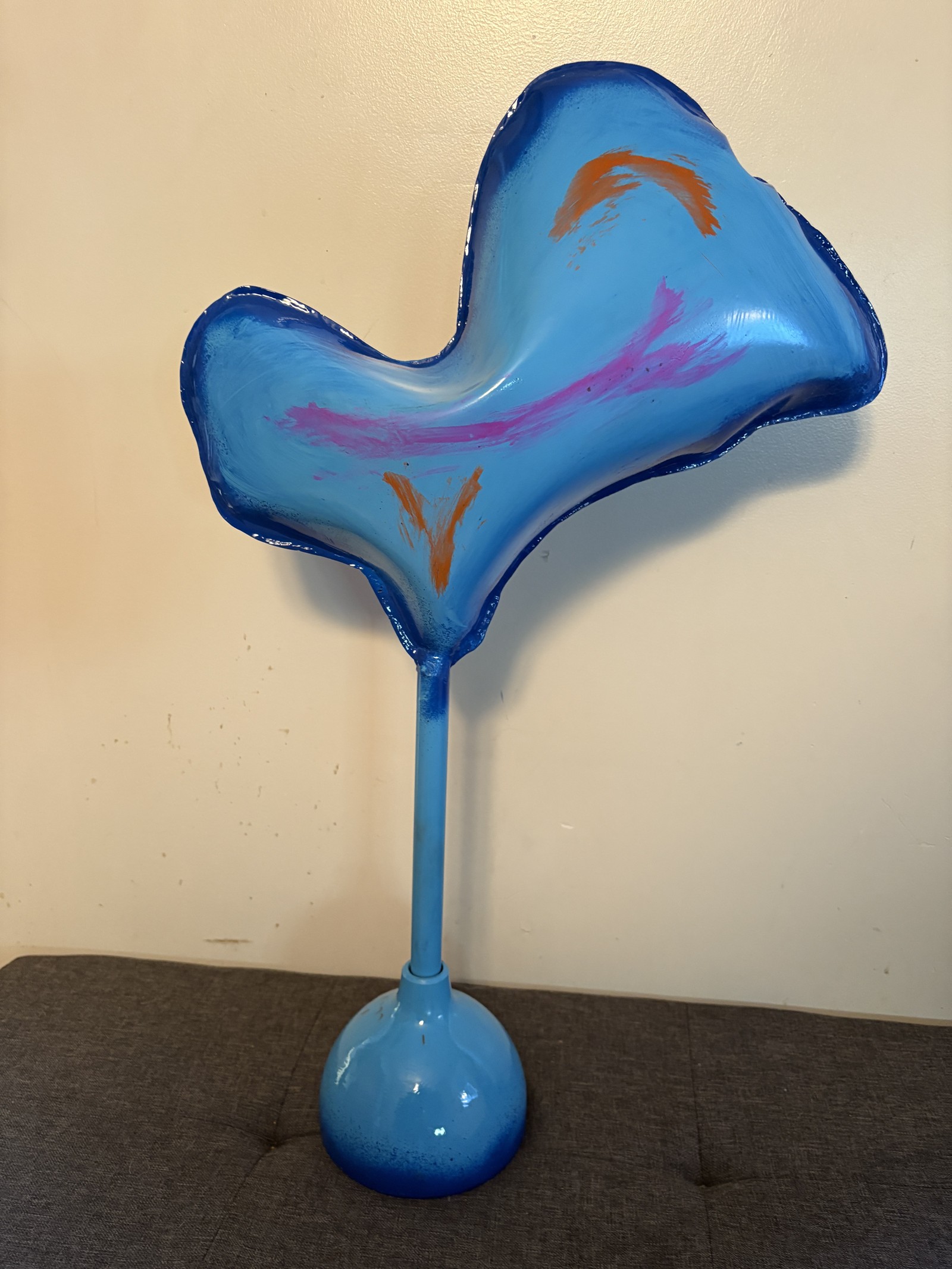 Abstract birdlike metal sculpture titled 'Space Chicken,' featuring a vibrant blue body with pink and orange streaks. Handcrafted by Saskatoon metal artist Rik Luczka, this unique tabletop sculpture is mounted on a slender blue stem and round base. A playful example of Saskatchewan-made fine art, showcasing creative metal forming and colorful finishes. Available for purchase or as inspiration for custom whimsical metal art commissions in Saskatoon.