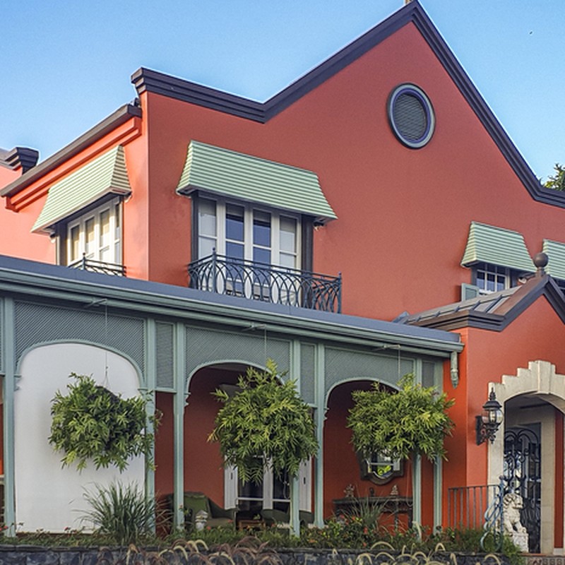Oblique angle shot showing new custom awnings, coloured in light green, installed over the windows of a 2-story orange house, coloured in burnt orange.