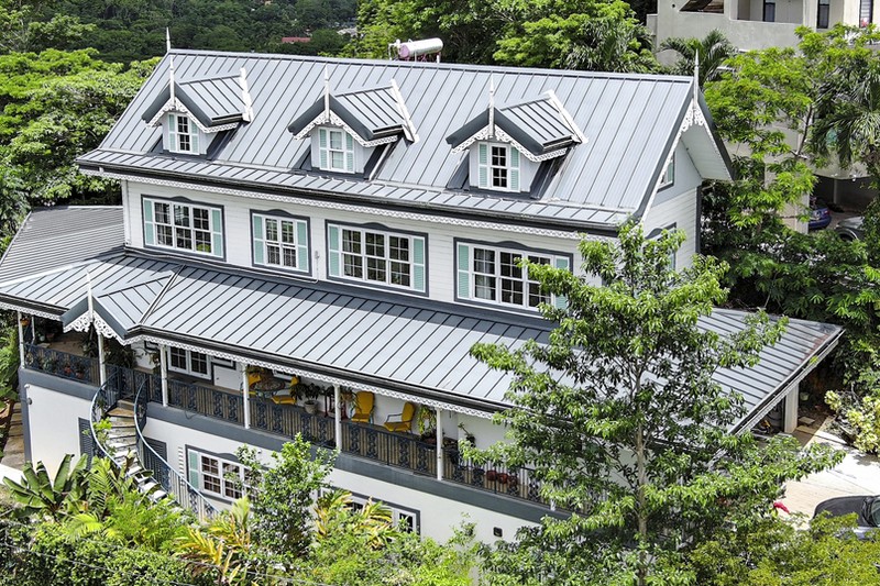 Aerial shot of a large, newly renovated house surrounded by greenery, with white walls, grey roofing, and mint green window shutters.