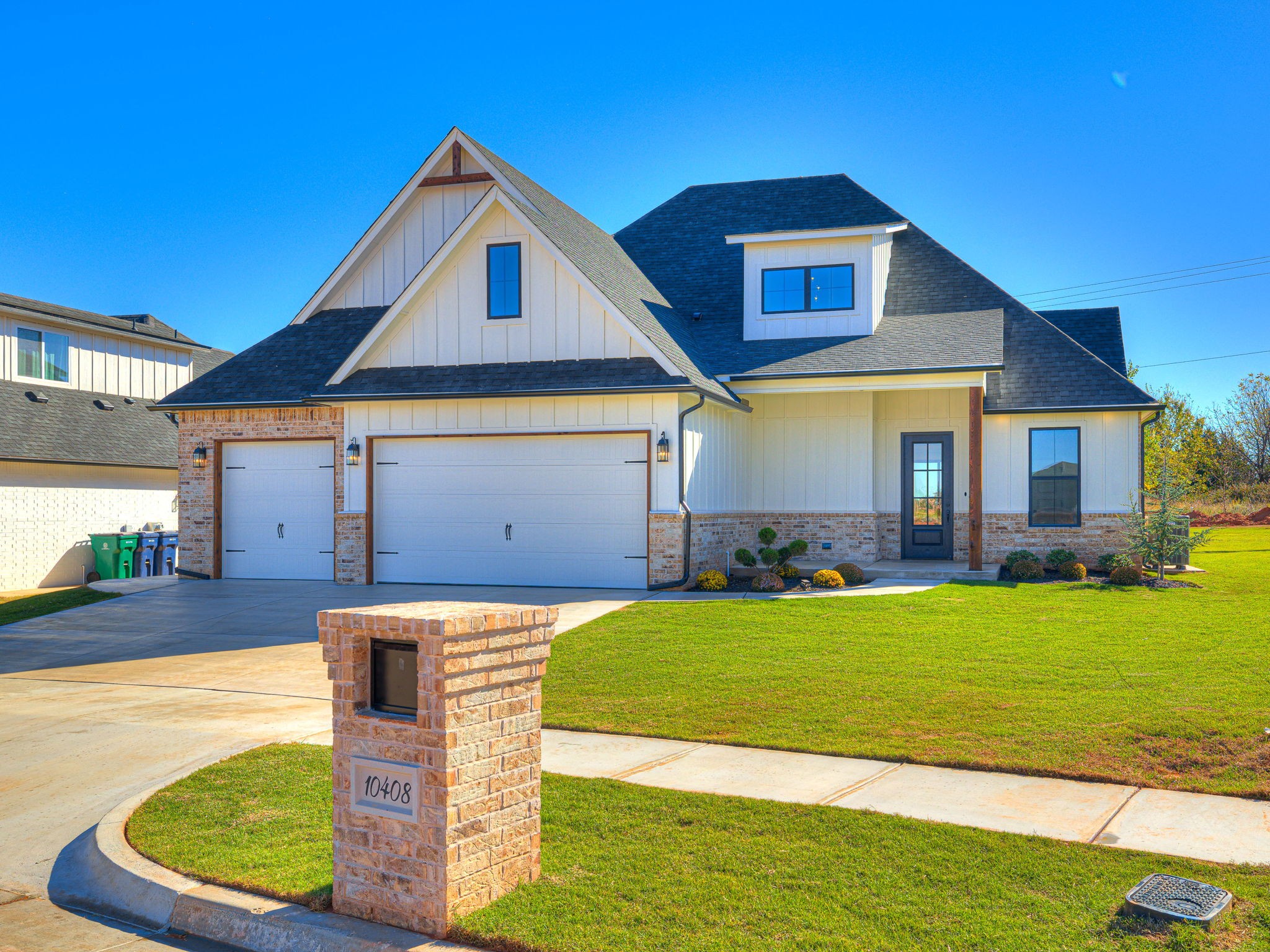 Front view of the custom home at 10408 SW 51st Street in Mustang Oklahoma showing the three-car garage, landscaped yard, and modern farmhouse design.