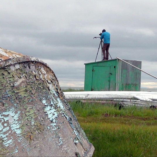 Derek Coté shooting video in Shishmaref, Alaska with old wooden boat in foreground