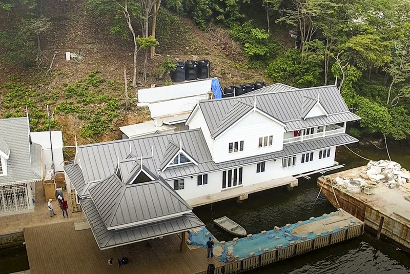 Aerial shot of a large island house with white walls and a grey roof being renovated.