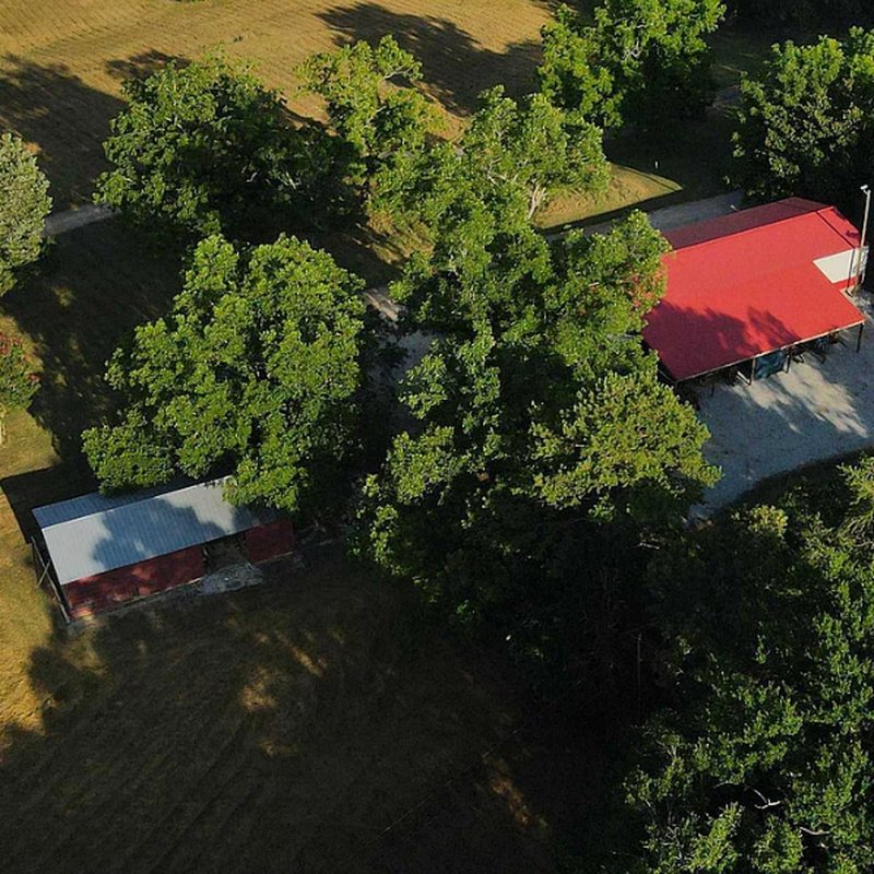 Close-up aerial view of the 100x32 multipurpose building with distinctive red roof and the 6-bay horse stable