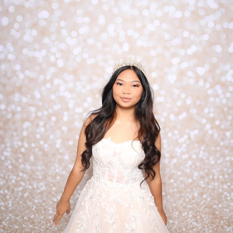 A young woman in a white gown and tiara posing at her 18th birthday in Virginia Beach with the VA Shoreline Events luxury photo booth backdrop