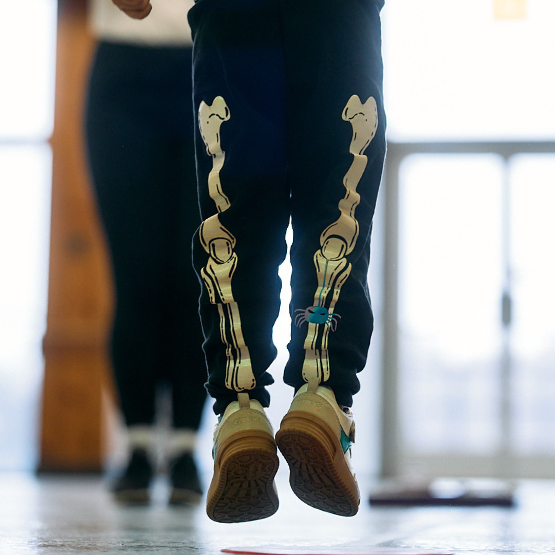 A hip hop student in skeleton leggings and sneakers jumps in the air.