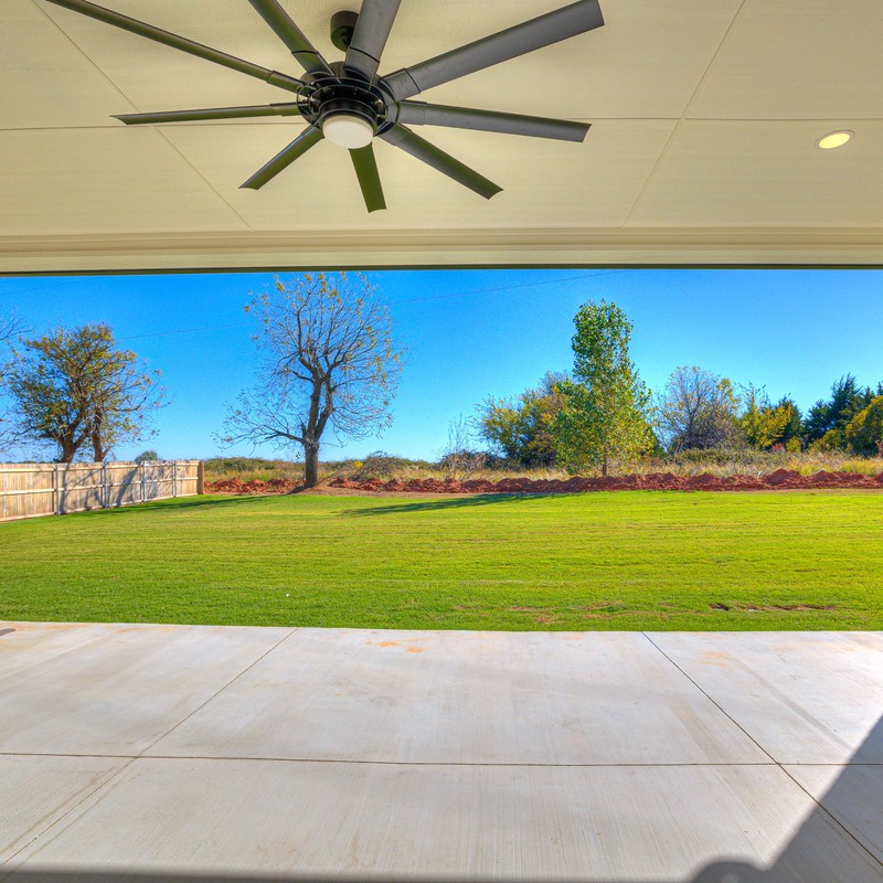 View from the covered patio with ceiling fan looking out onto the spacious fenced backyard of the Mustang Oklahoma custom home.
